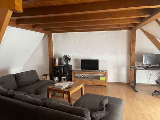 Living room with wooden beams, grey sofa, coffee table, TV stand, fan, bookshelf, and a small table with a chair.