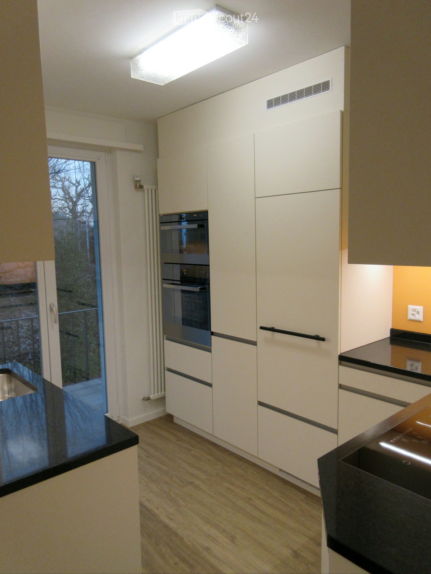 Modern kitchen with white cabinets, black countertops, and a built-in oven. Features a large window with a view of the garden.