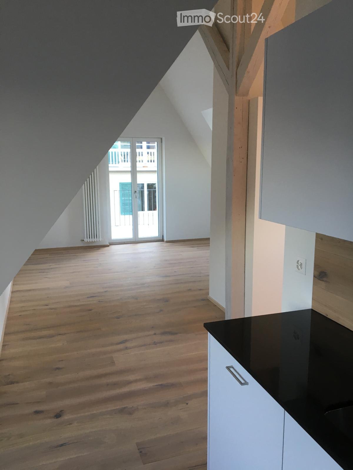 An unfurnished attic room with wooden flooring, white walls, and a sliding glass door leading to a balcony.