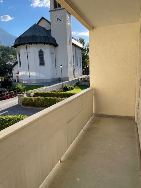 Balcony overlooking a white church with a clock tower, surrounded by greenery and a clear blue sky.