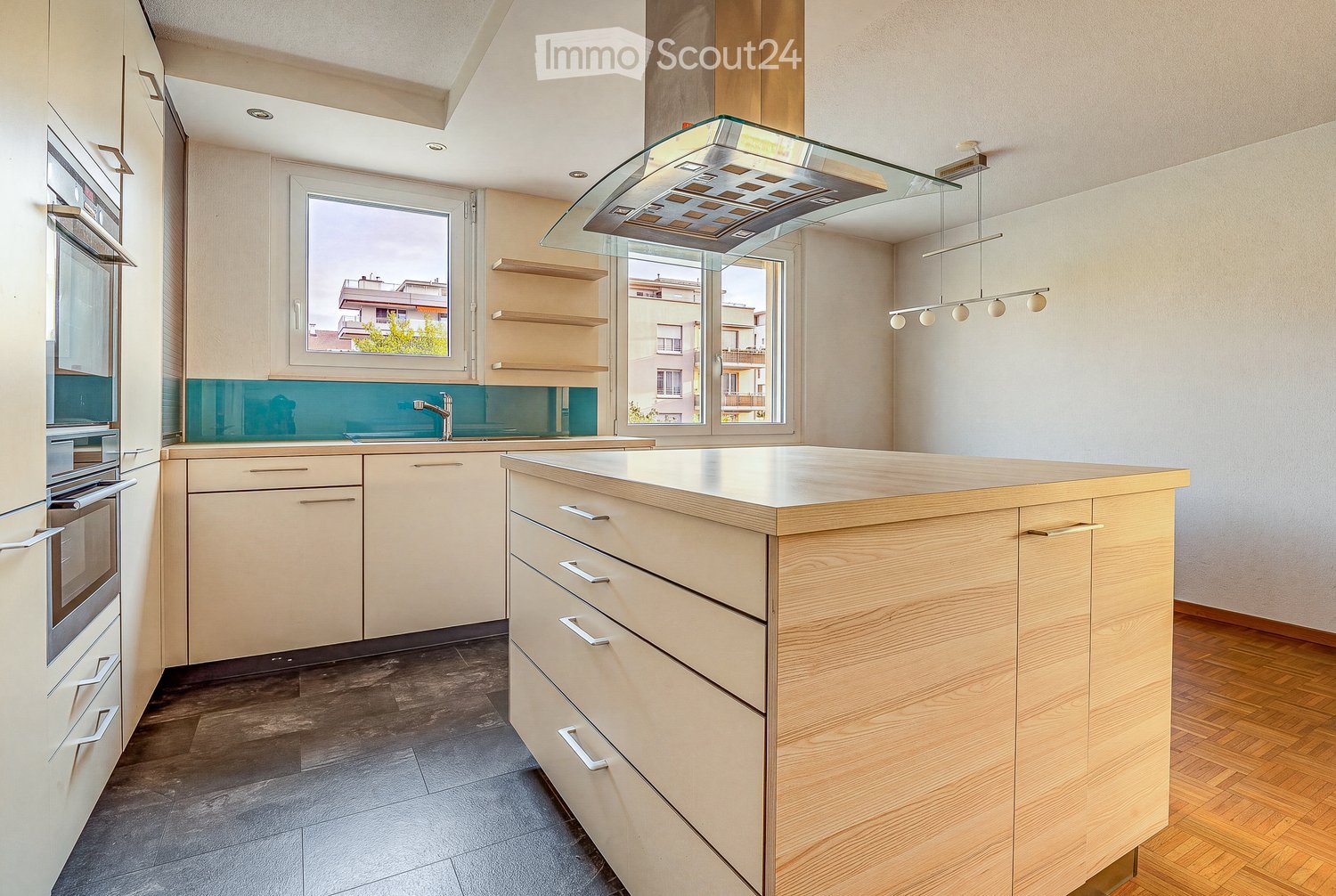 Modern kitchen with light wood cabinets, a central island, stainless steel appliances, and pendant lighting.