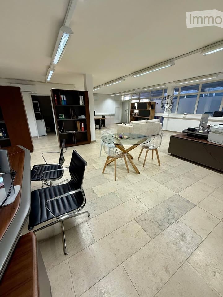 Modern office space with a glass table, chairs, a sofa, bookshelf, and office equipment.