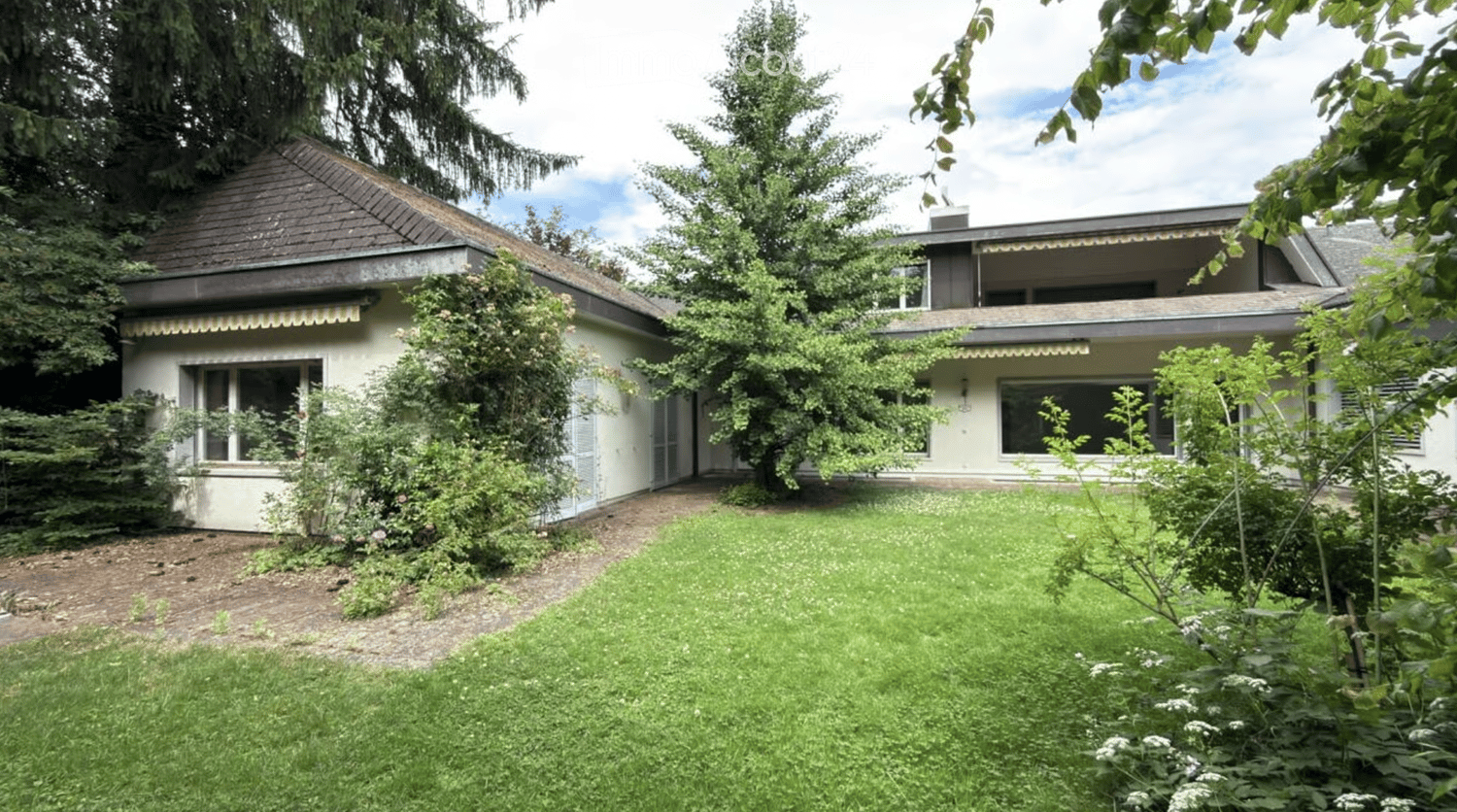 Two-story house with a pitched roof, surrounded by greenery and a well-maintained lawn.