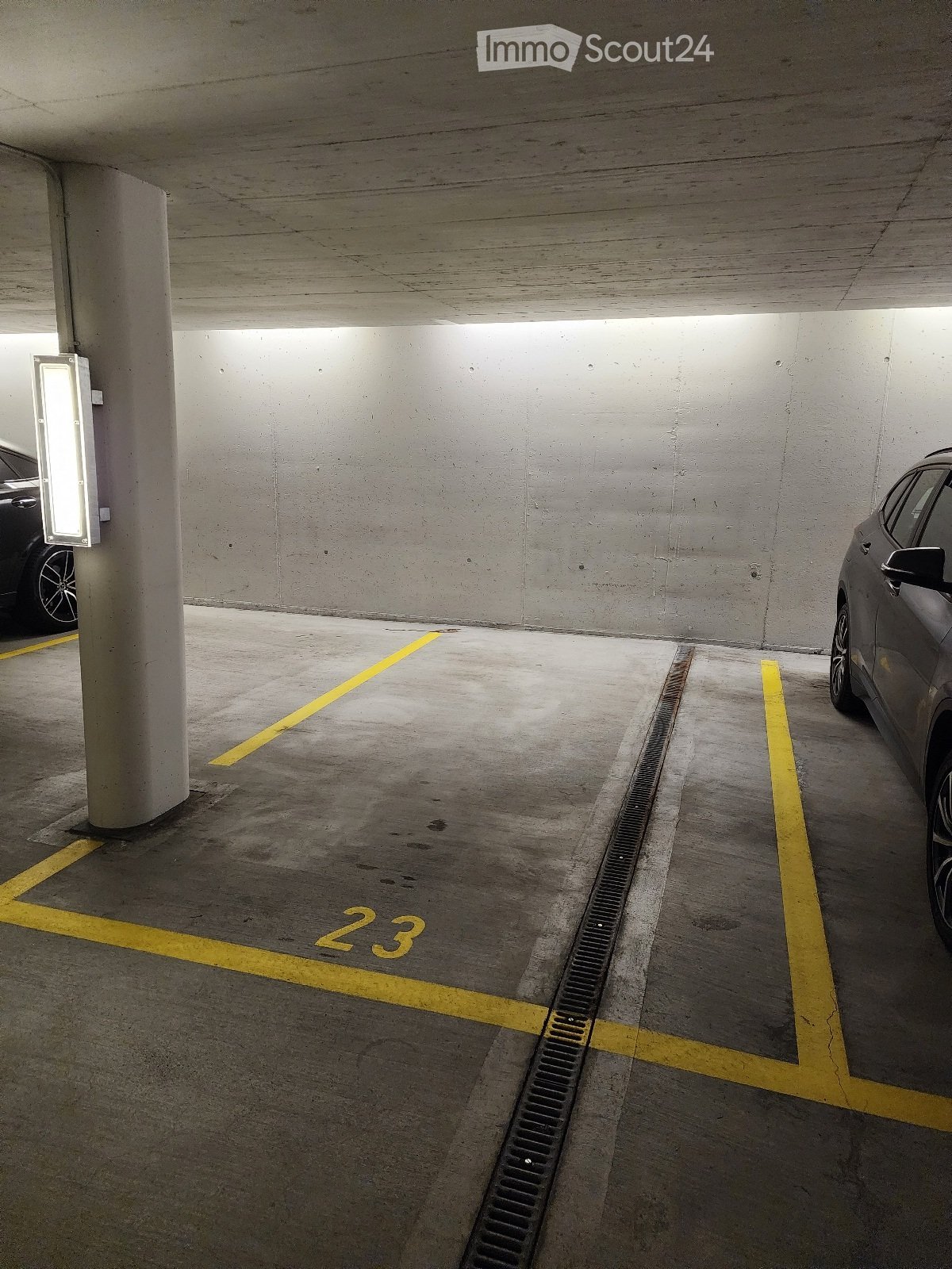 Underground parking area with marked parking spaces, concrete pillars, and two parked cars visible in the background.