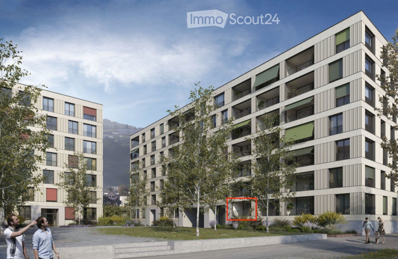 Modern multi-story residential building with balconies and green awnings, surrounded by trees and a paved area.