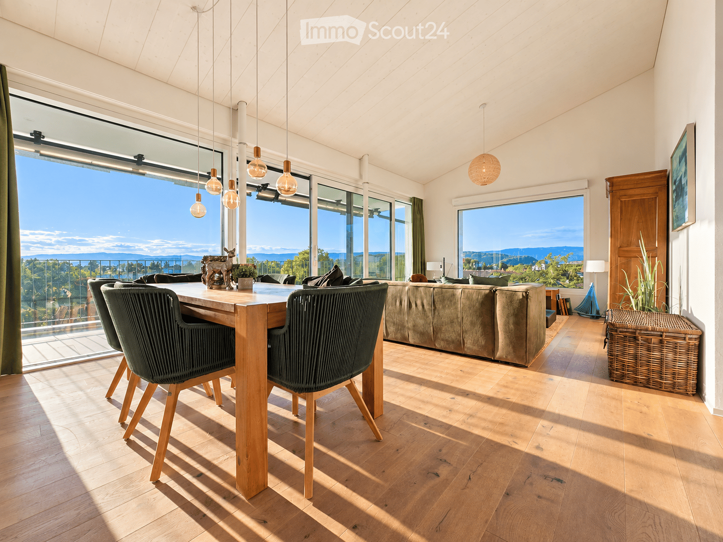 Bright living and dining area with large windows offering scenic views, wooden flooring, a sofa, dining table with chairs, and decorative items.