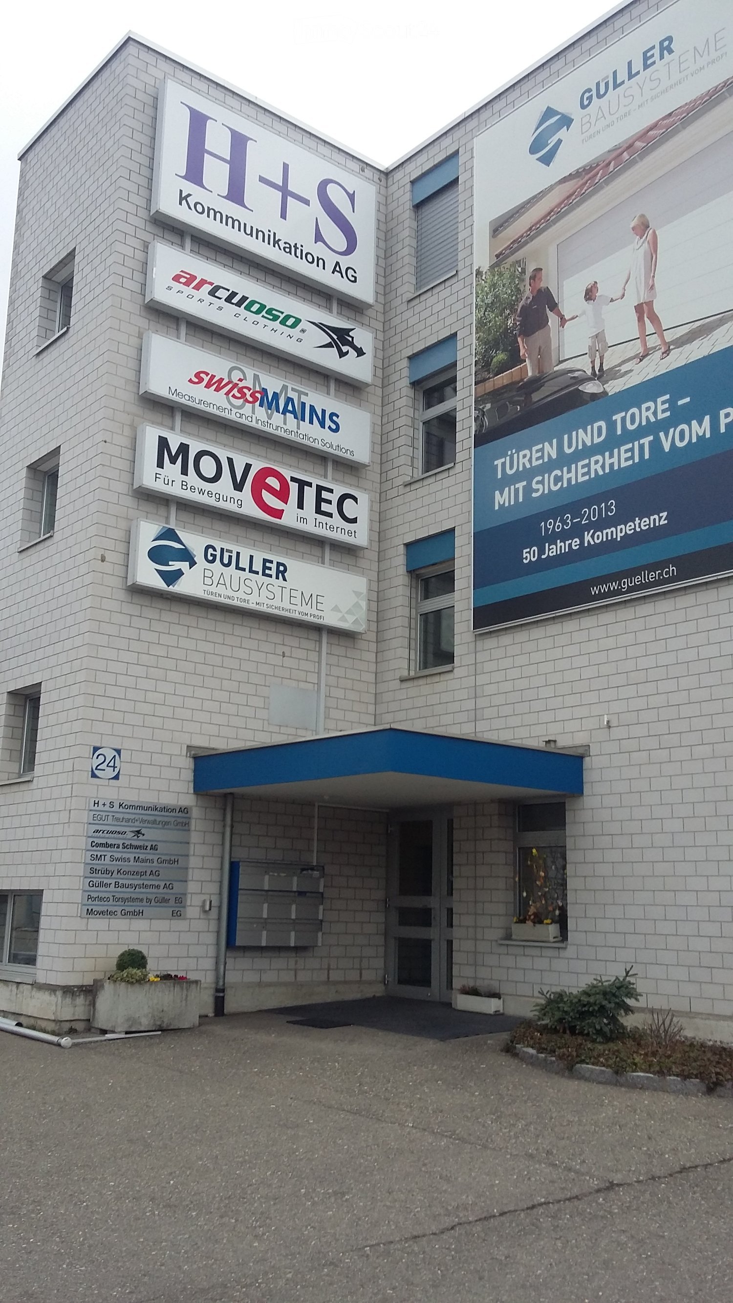 A multi-story building with a brick facade, multiple company signs, and a blue awning over the entrance.