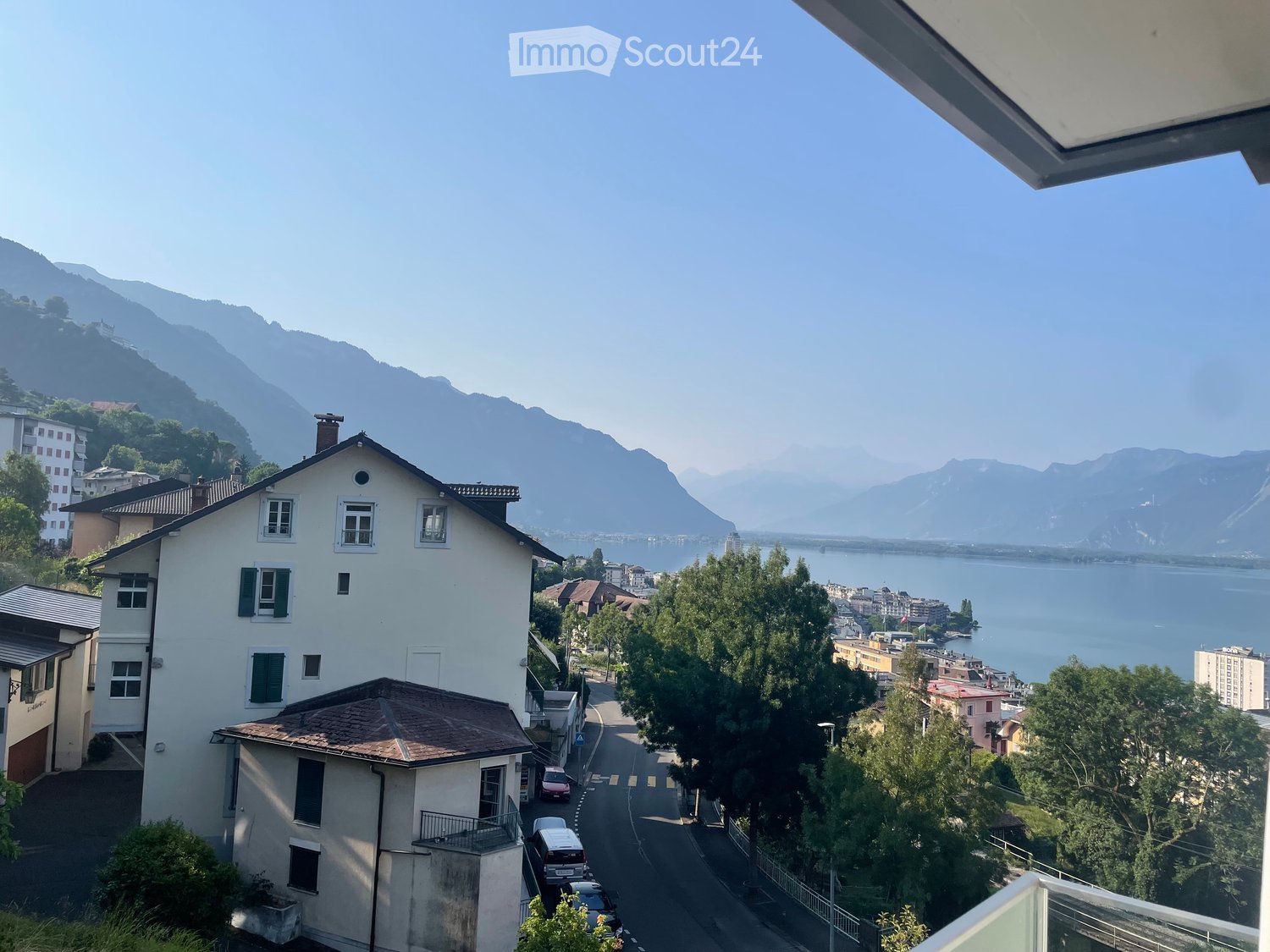 Balcony view overlooking a town with houses, a lake, and distant mountains.