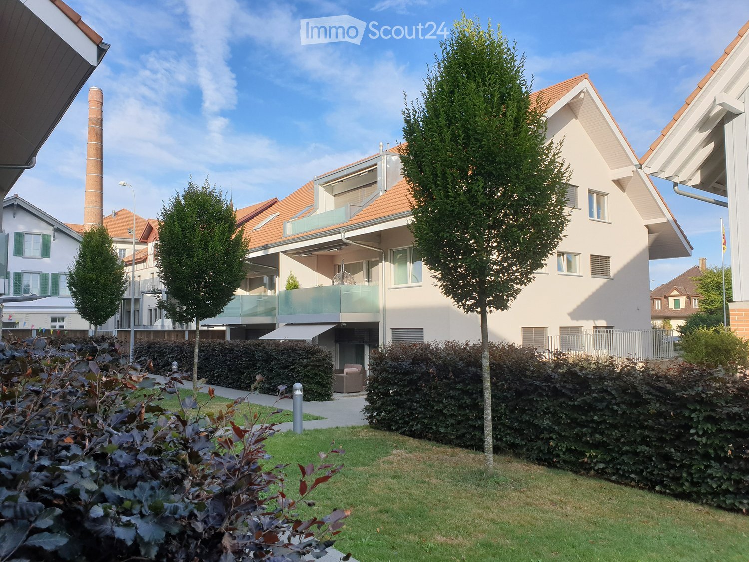 white building, brown roof, balcony, trees, grass, pathway, metal fence
