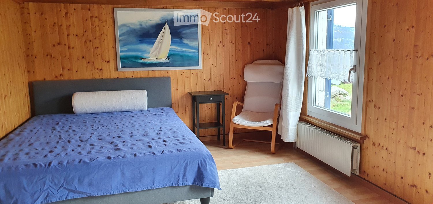 Cozy wooden bedroom with a double bed, nightstand, armchair, and a painting of a sailboat on the wall.