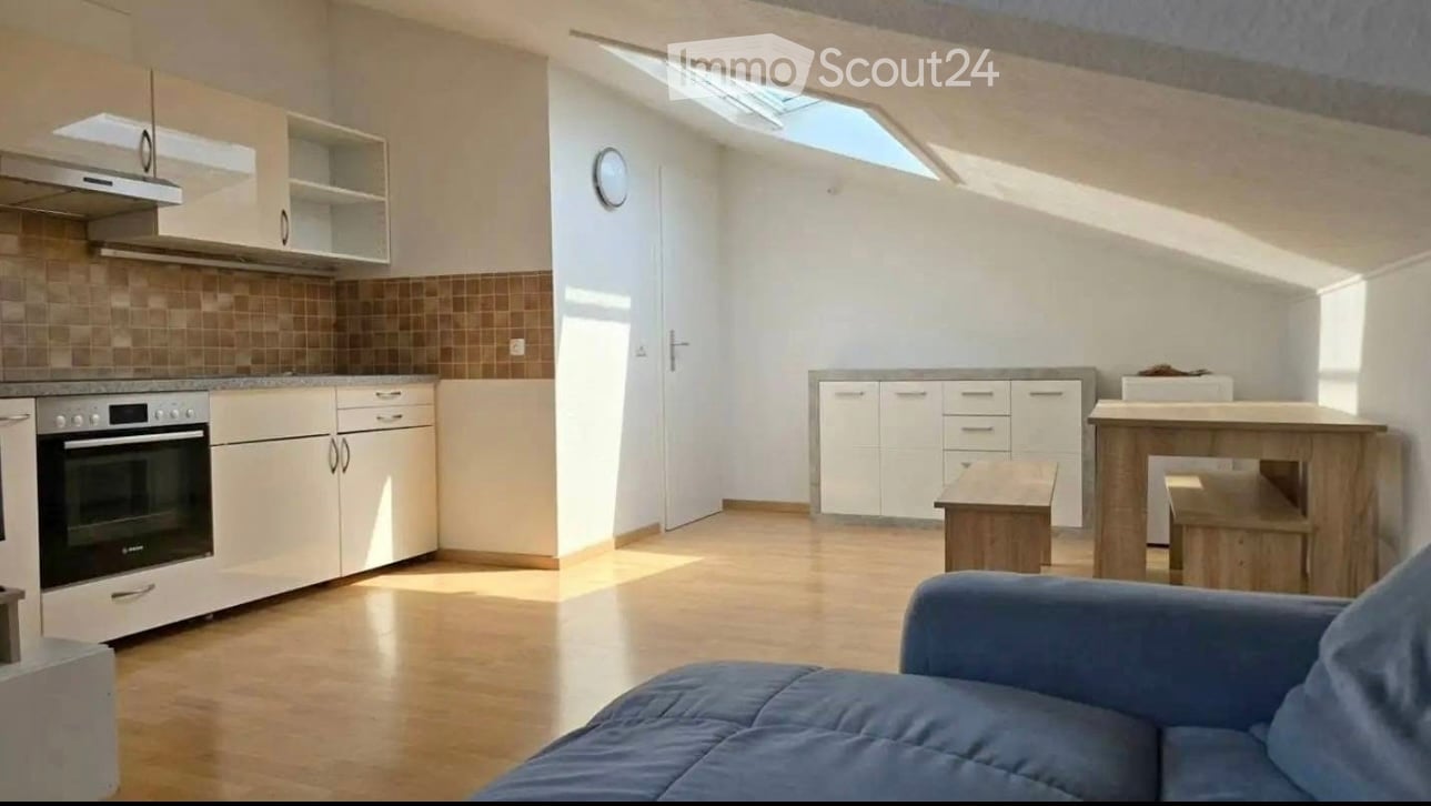 Bright, open-plan living and kitchen area with wooden flooring, white cabinets, a blue sofa, a wooden kitchen island, and a small wooden stool.