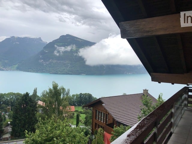 Balcony overlooking a scenic lake and mountain landscape with a wooden railing and tiled floor.