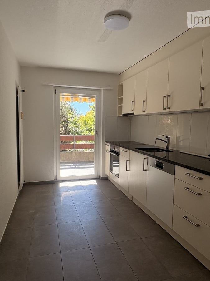 Modern kitchen with white cabinets, dark countertops, and a sliding glass door leading to a balcony. Features include a sink, faucet, oven, and dishwasher.