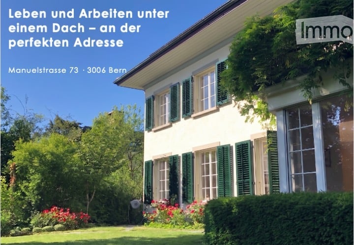 A two-story house with white walls, green shutters, and a well-maintained garden with red flowers and green shrubs.