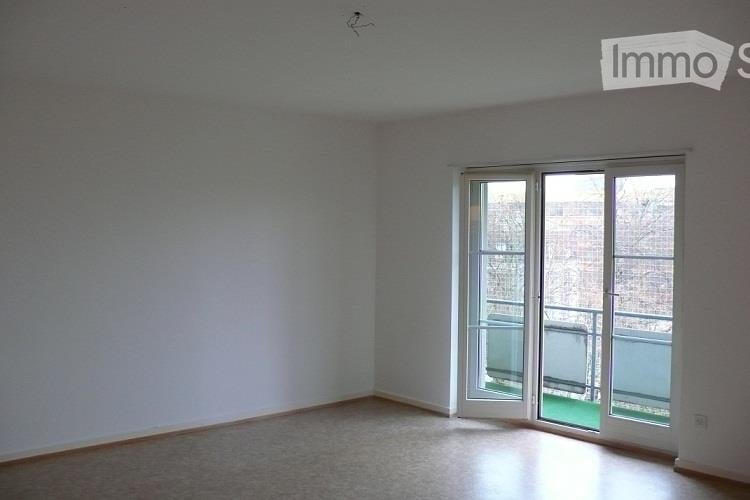 Empty room with light-colored walls, wooden floor, and large sliding glass doors leading to a balcony.