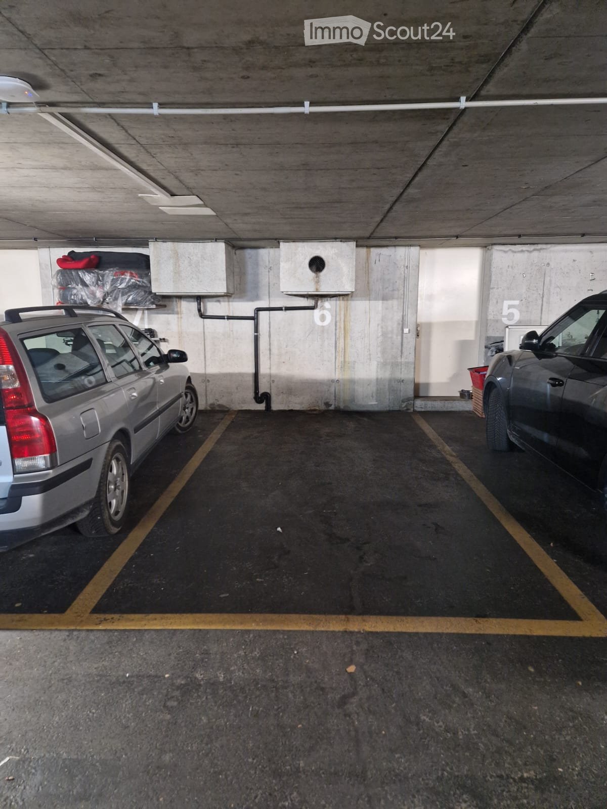 Underground parking area with two parked cars, marked parking spaces, and concrete walls.