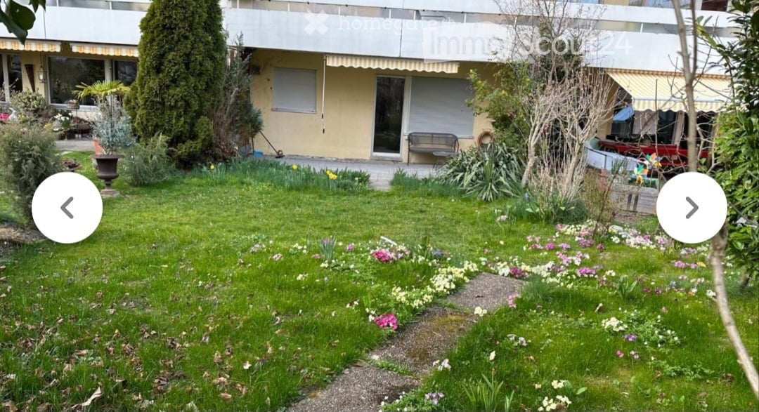Well-maintained garden with green lawn, colorful flowers, shrubs, and a small bench near the building entrance.
