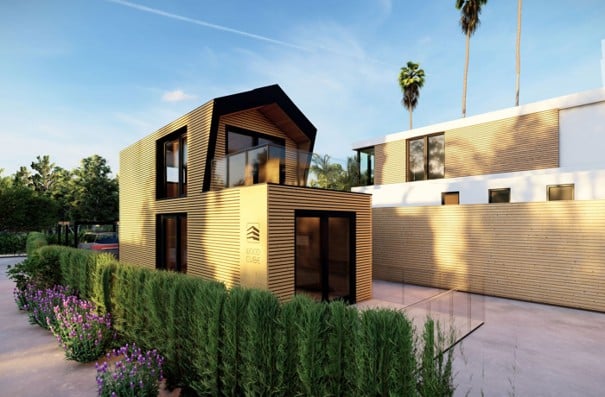 Modern two-story house with a contemporary design, featuring large windows, a flat roof, and a wooden facade. The house is surrounded by a well-maintained garden with shrubs and flowers, and there is a neighboring building visible in the background.