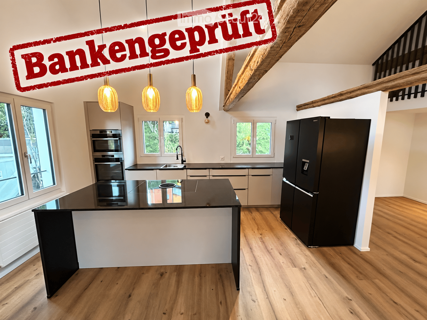 Modern kitchen with wooden flooring, white cabinets, black countertops, stainless steel appliances, and pendant lights.