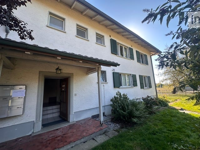 Two-story house with white exterior, green shutters, and a small garden area.