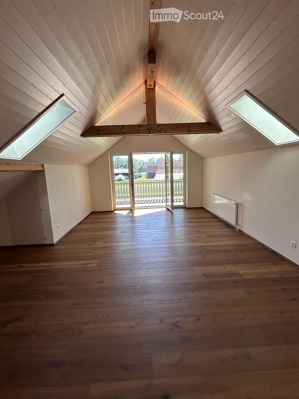 Empty room with wooden flooring, white walls, skylights, and a door leading to a balcony or outdoor area.