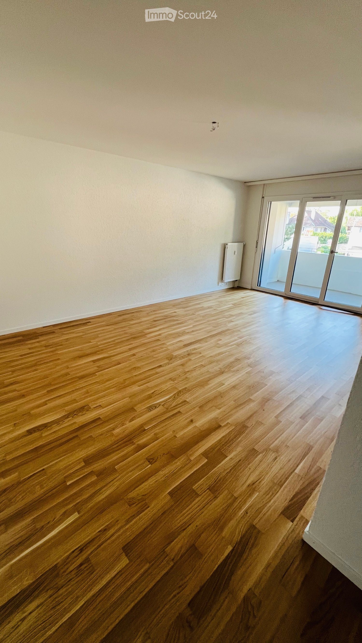Empty room with wooden flooring and white walls, featuring a sliding glass door leading to a balcony.