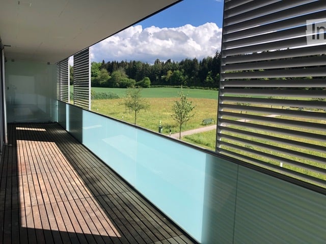 Modern balcony with wooden decking, glass railing, and scenic countryside view.