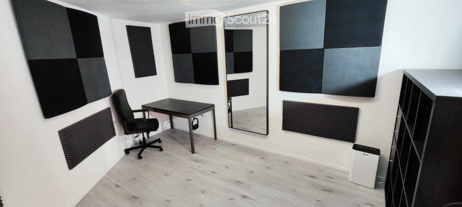 Modern, soundproofed room with a black desk, ergonomic chair, large mirror, and acoustic panels on the walls.
