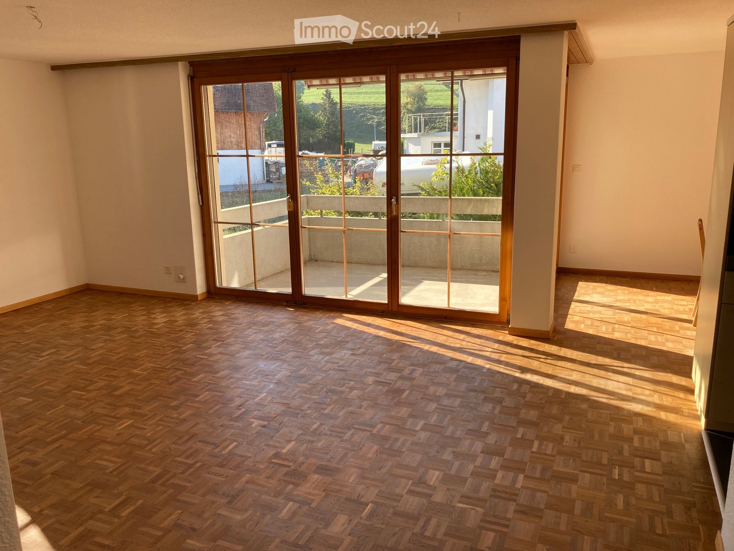 Empty room with wooden herringbone flooring and large sliding glass doors leading to a balcony or outdoor area.