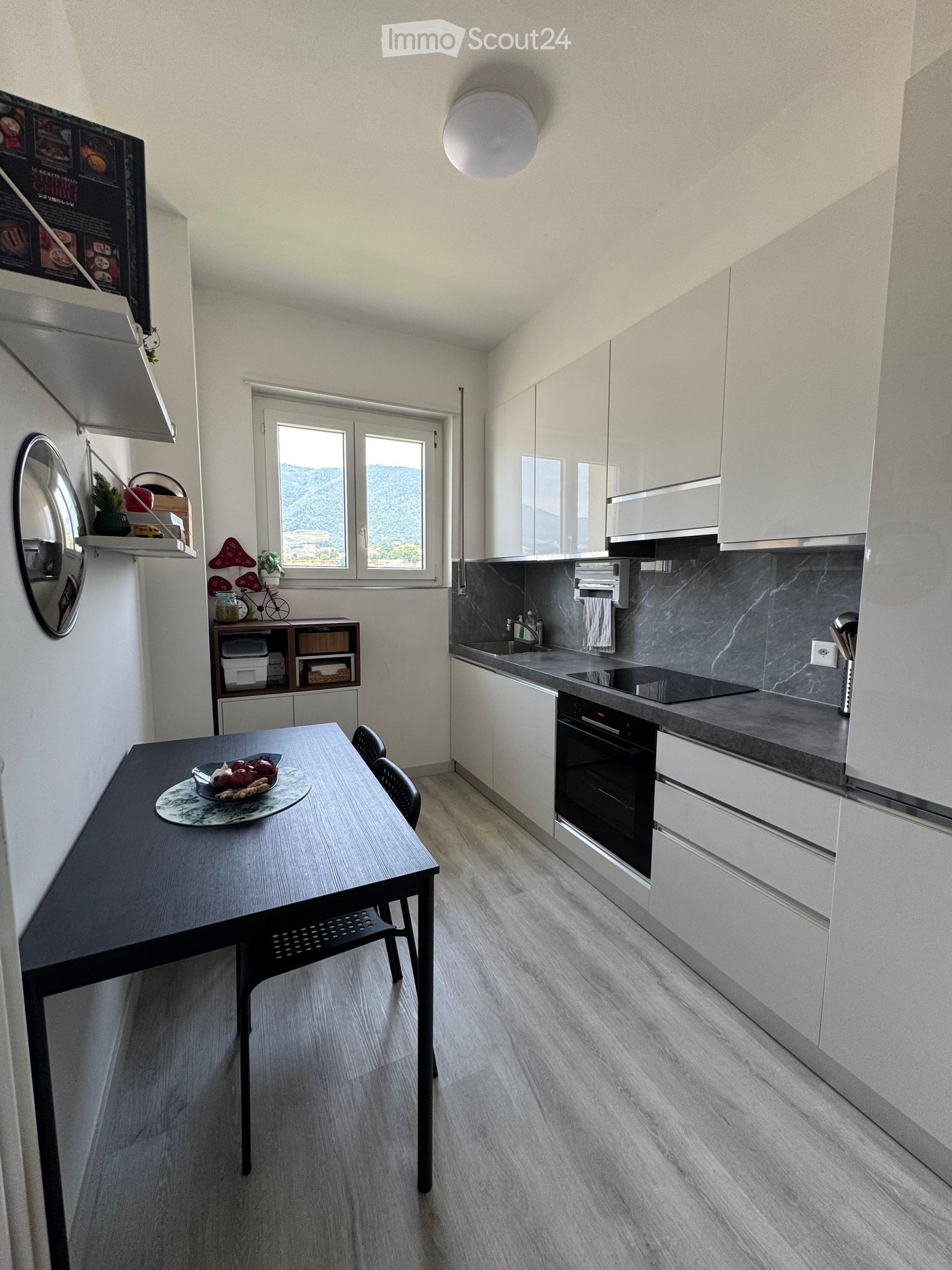 Modern kitchen with white cabinets, dark countertops, and a dining area featuring a table and chairs. The kitchen includes an oven, sink, and various appliances.