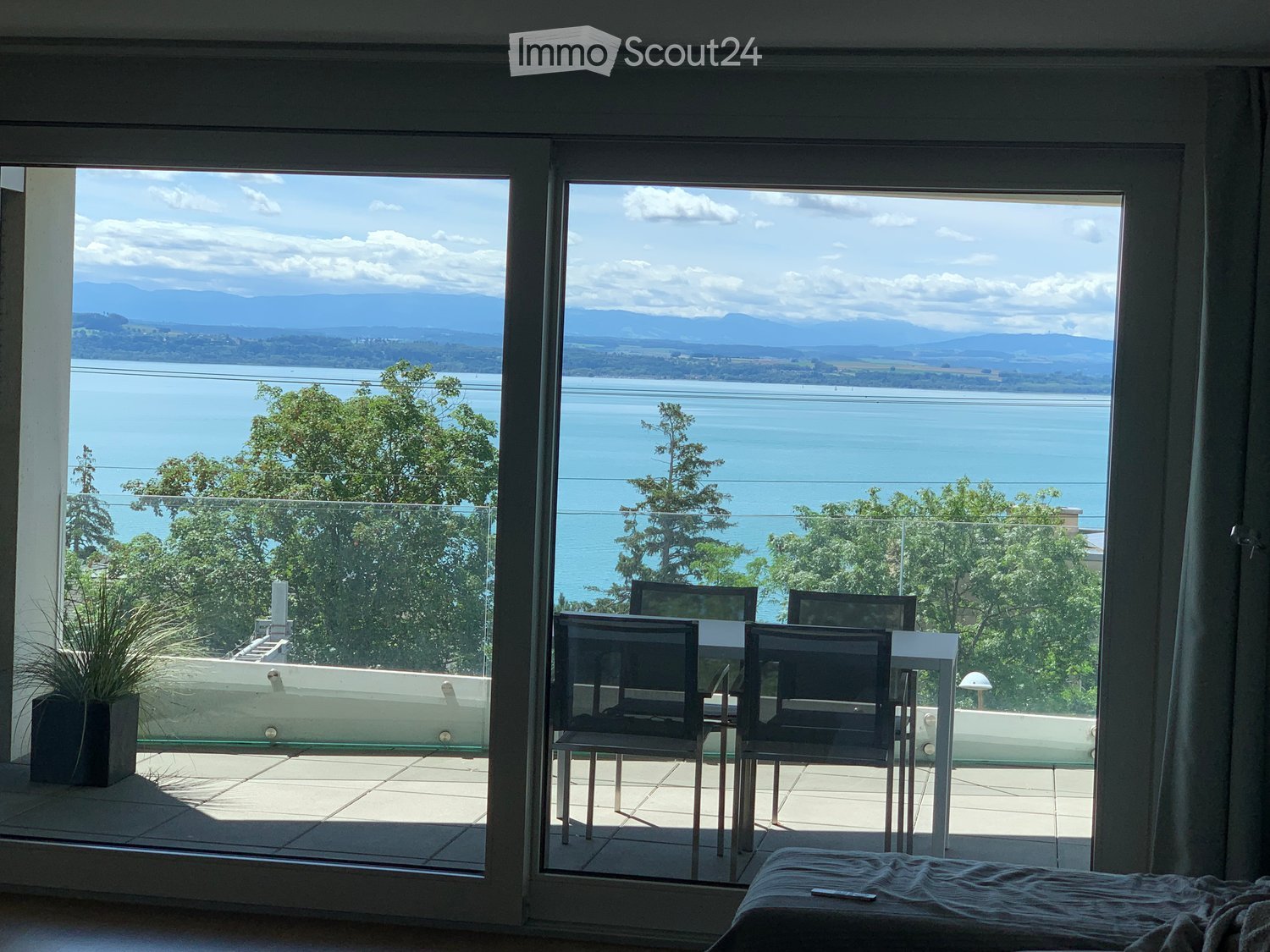 Balcony with a scenic view of a lake and mountains, featuring a small table and chairs, and a potted plant on the adjacent balcony.