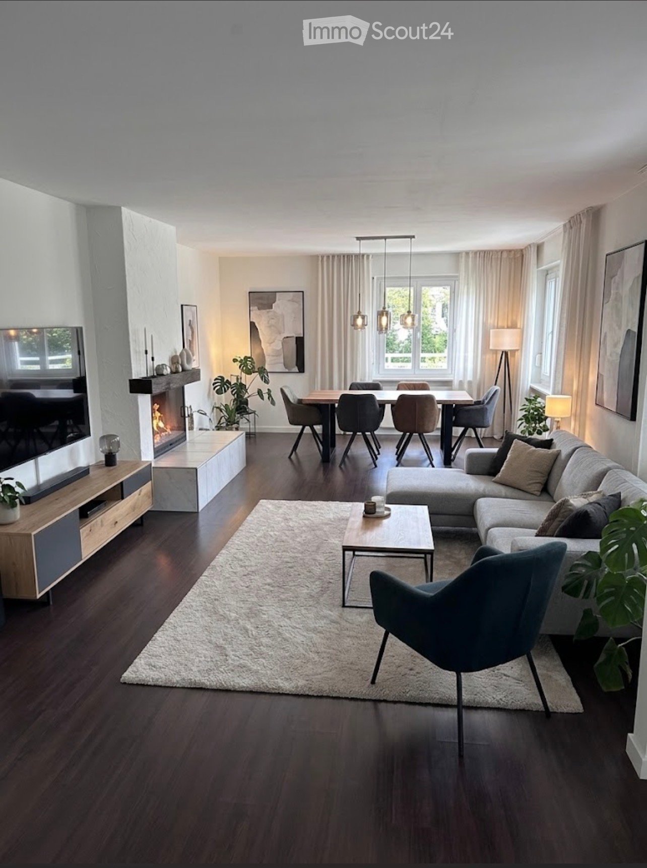 Modern living room with a sectional sofa, coffee table, dining area, fireplace, and large windows with curtains.