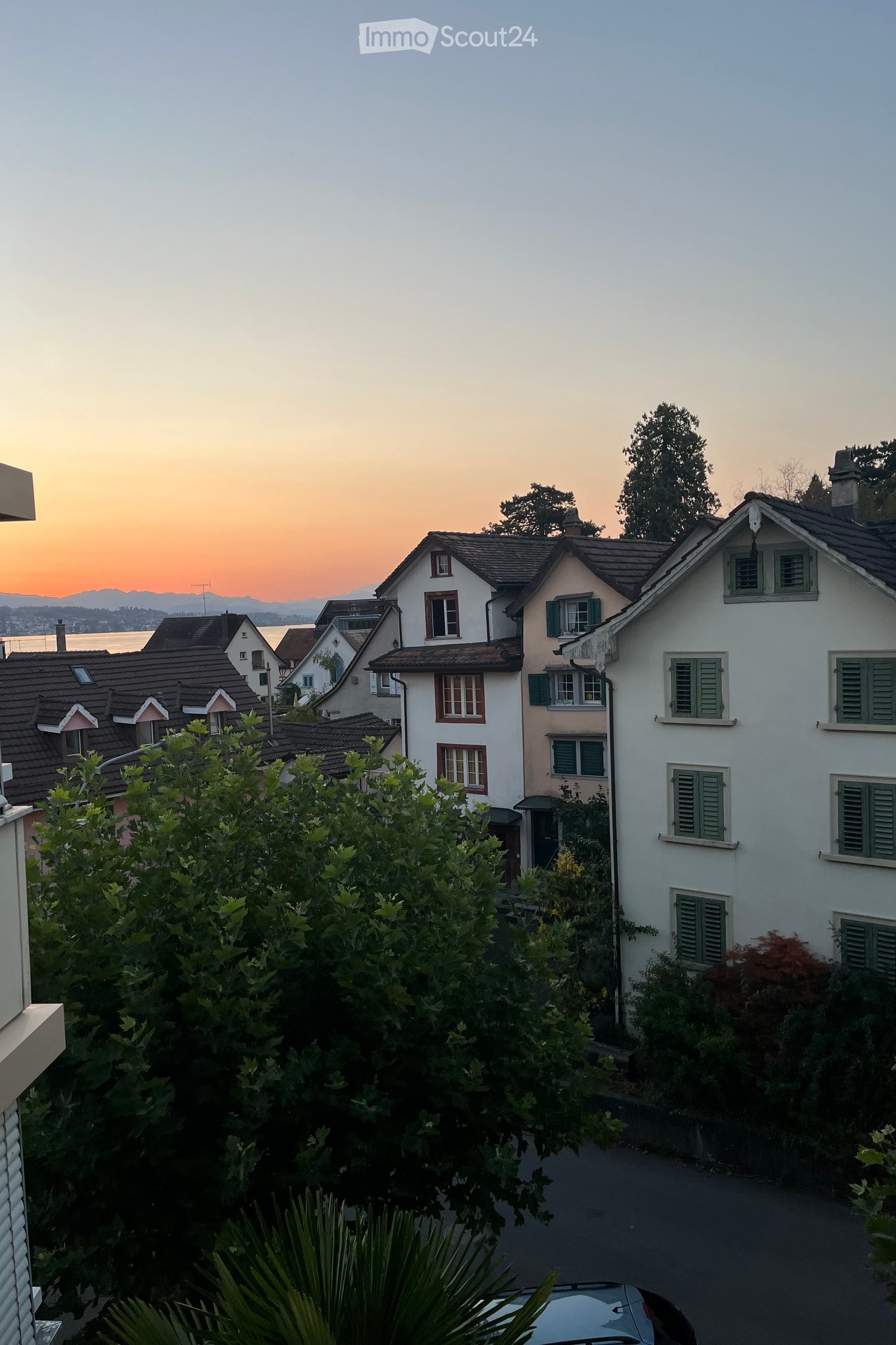 Residential neighborhood with multiple houses, green shutters, and a view of the lake and mountains at sunset.
