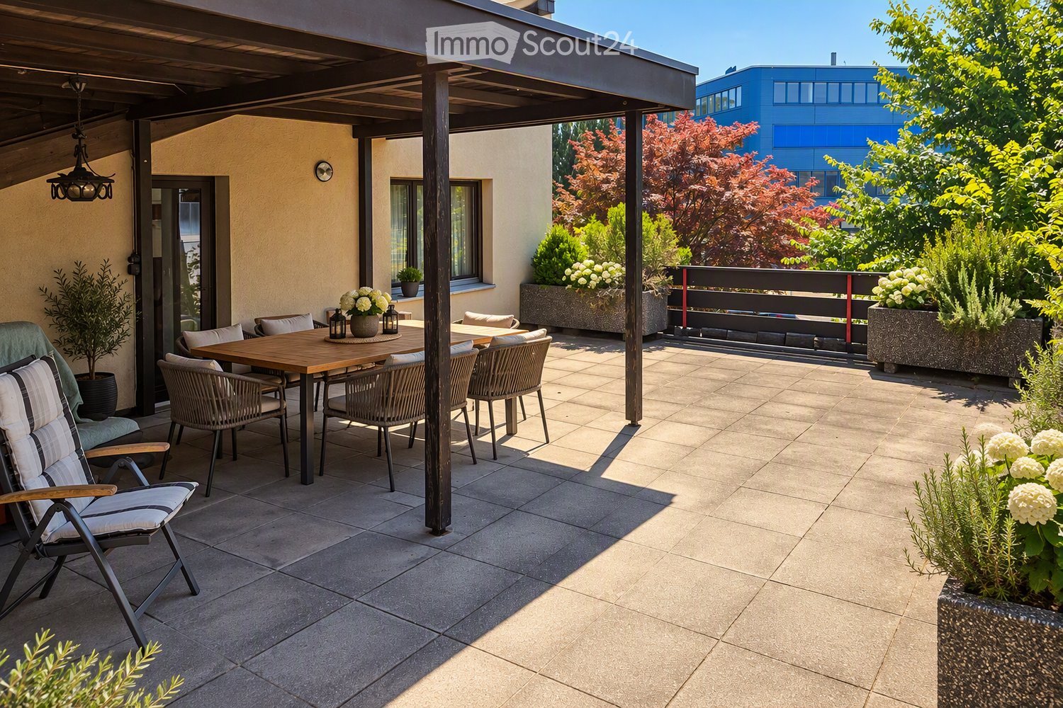 A modern outdoor patio with a wooden table, chairs, potted plants, and lanterns, featuring a tiled floor and a covered area with wooden beams.