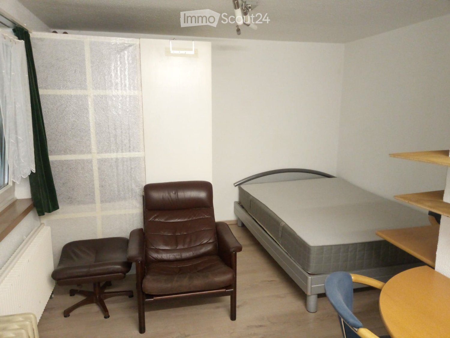 Small bedroom with bed, armchair, ottoman, shelf, desk, and chair