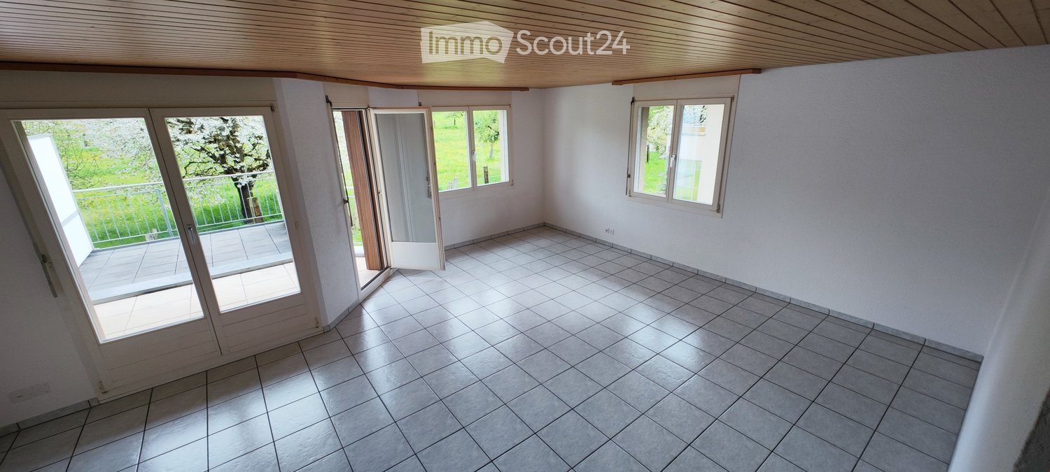 Empty room with tiled floor, white walls, large windows, and sliding glass doors leading to a balcony.