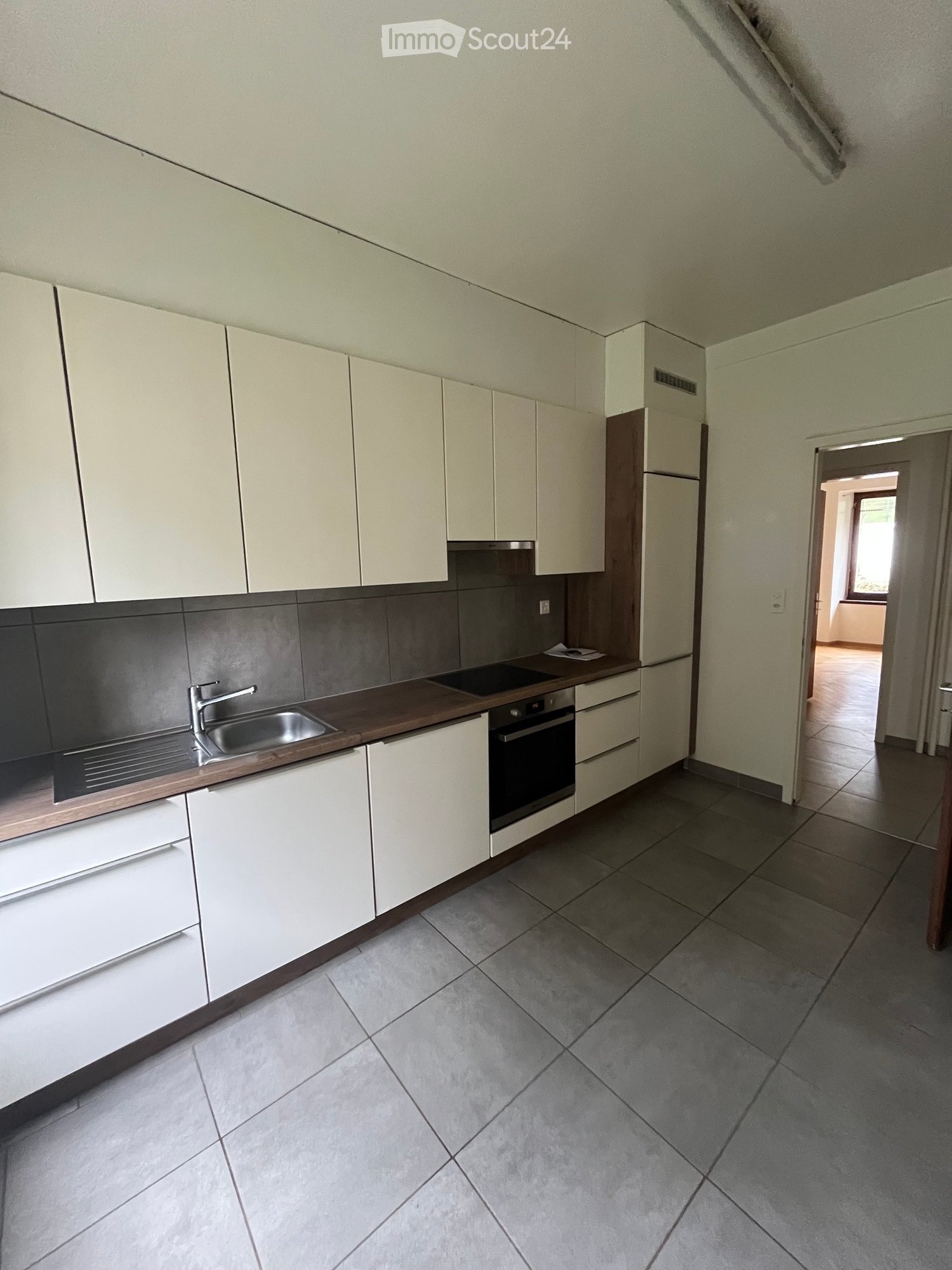 Modern kitchen with white cabinets, stainless steel sink, and oven. Grey tiled backsplash and grey tiled floor.