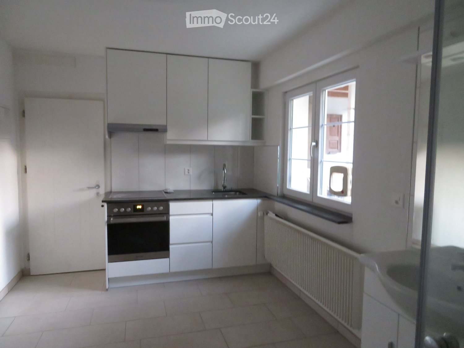 Modern kitchen with white cabinets, stainless steel oven, sink, and faucet. Features tiled floor and large windows.