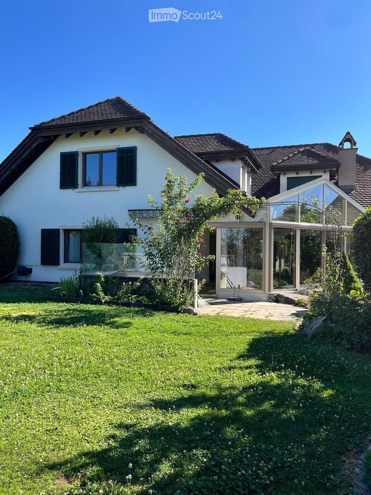Two-story house with white exterior, green shutters, and a well-maintained garden with a patio area.