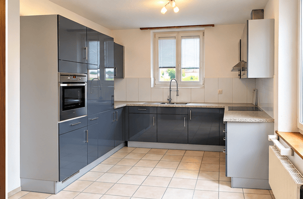Modern kitchen with grey cabinets, stainless steel oven, sink, and countertop. Natural light from a window above the sink.