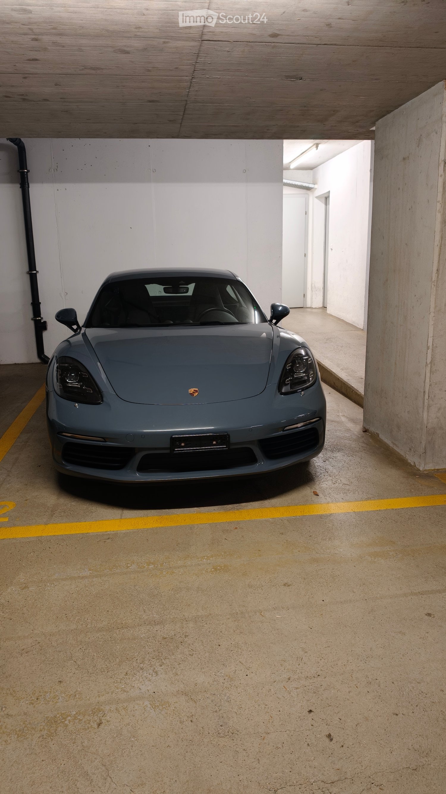 Underground garage with a single grey sports car parked inside, concrete floor, white walls, and a wooden ceiling.