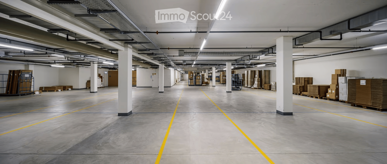 Large, empty warehouse or industrial space with concrete floors, white walls, and visible storage racks and pallets.