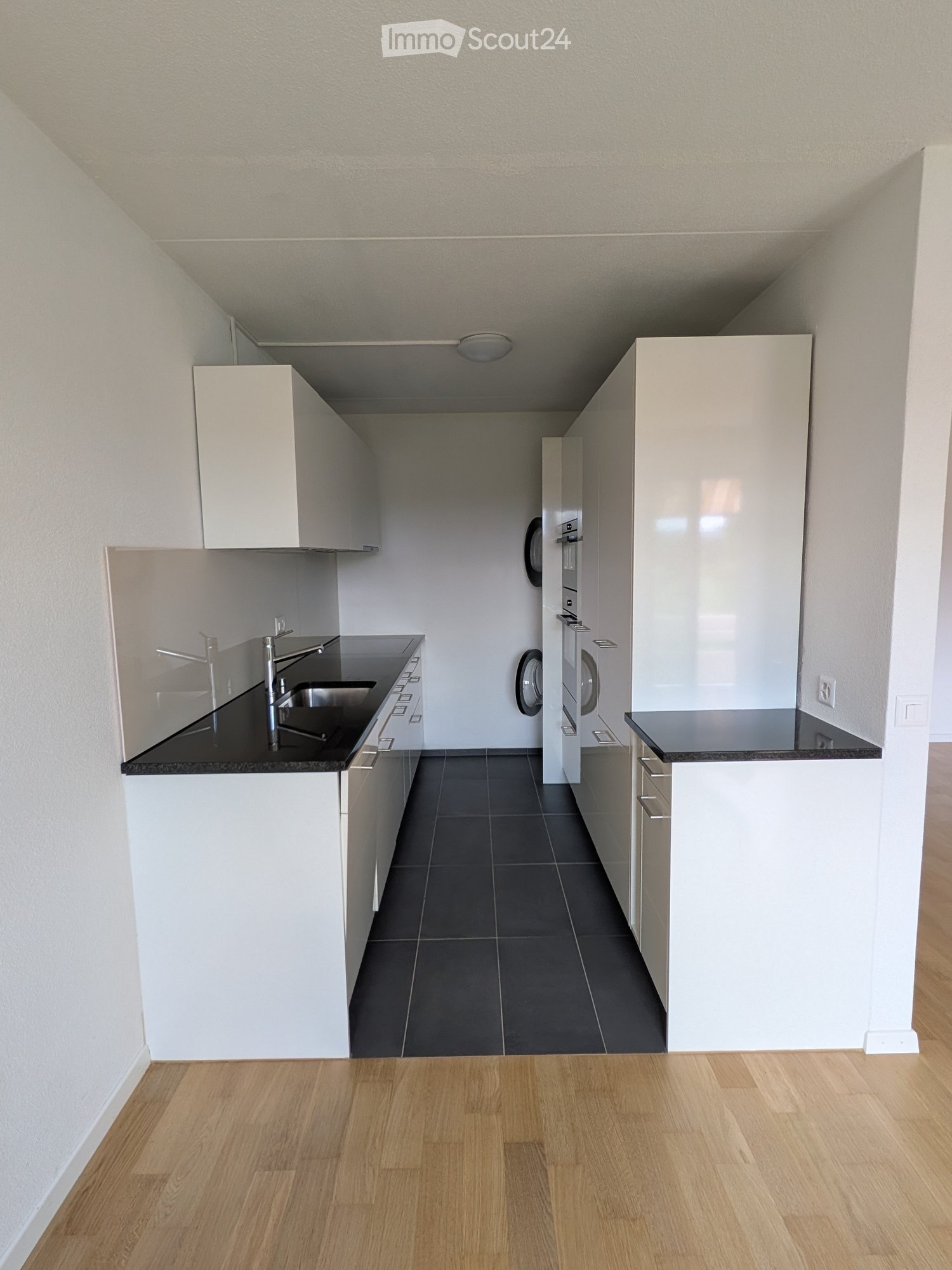 Modern kitchen with white cabinets, black countertops, stainless steel sink, and a washing machine in the background.