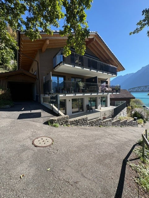 Modern two-story house with balconies, large windows, and a scenic mountain view. Features a garage and a driveway.