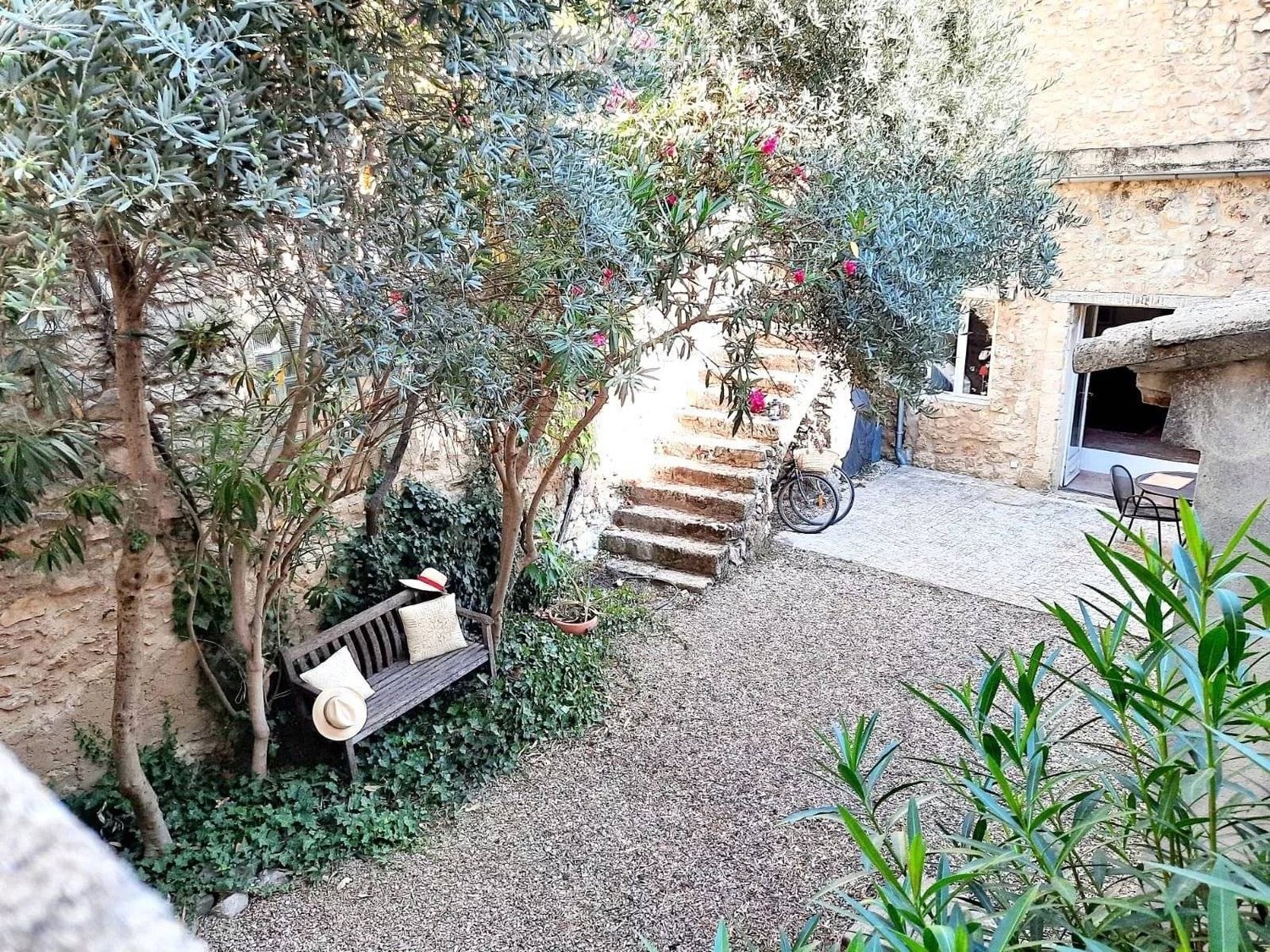 a cozy garden with bench, trees, greenery, stone pathways, and stone house in the background