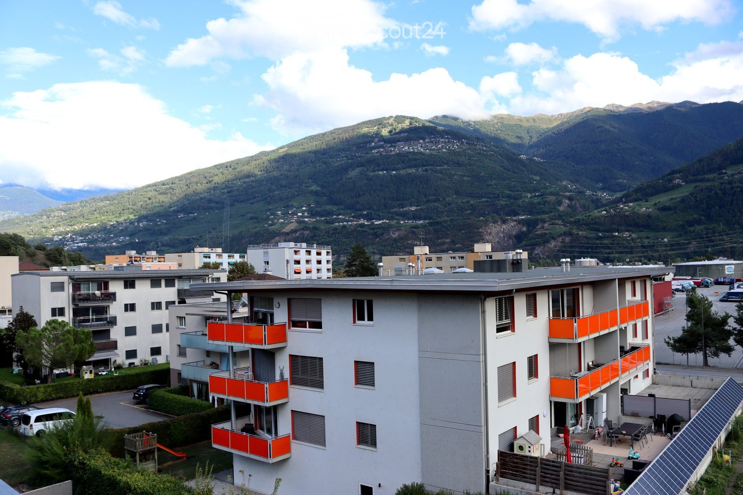 Multi-story residential building with orange balconies, surrounded by other buildings and a mountainous backdrop.