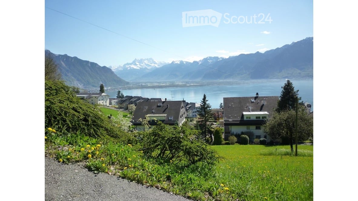 Scenic view of a lakeside town with houses, green fields, and distant mountains.