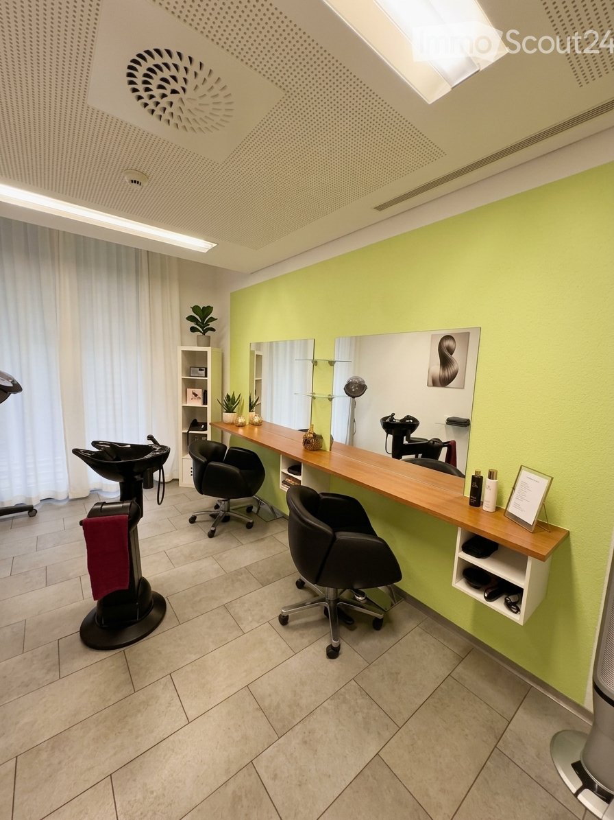 Modern, well-lit salon with light green walls, wooden counter, black chairs, mirrors, shelves, and decorative plants.