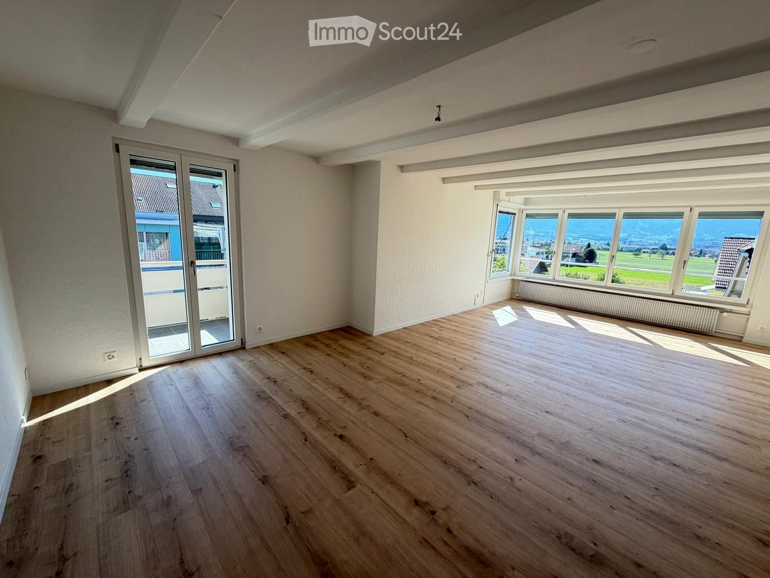 Empty room with wooden flooring, large windows, and a sliding glass door leading to a balcony.