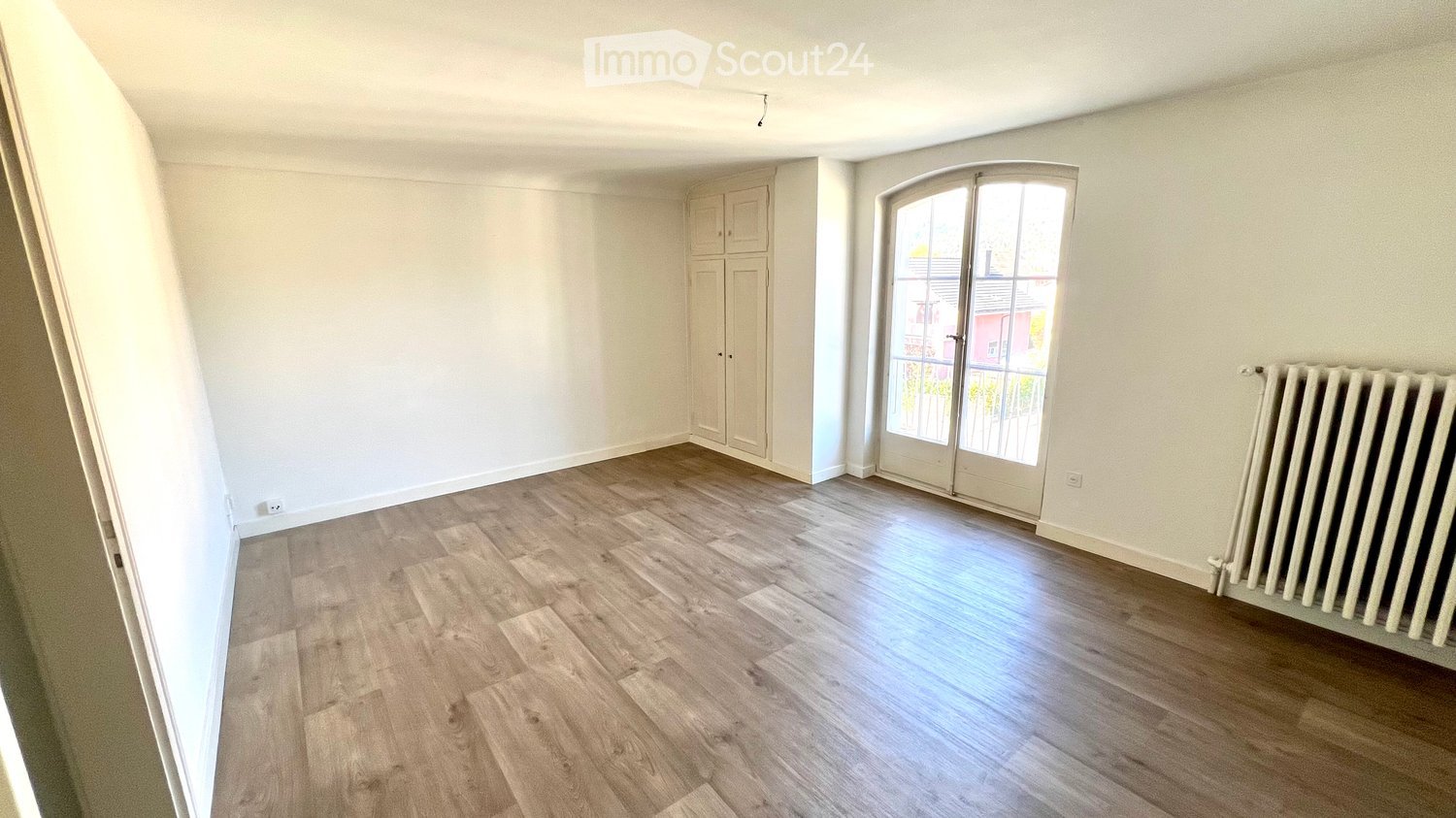 Empty room with light wooden flooring, white walls, a built-in closet, and a large window with glass doors leading to a balcony.